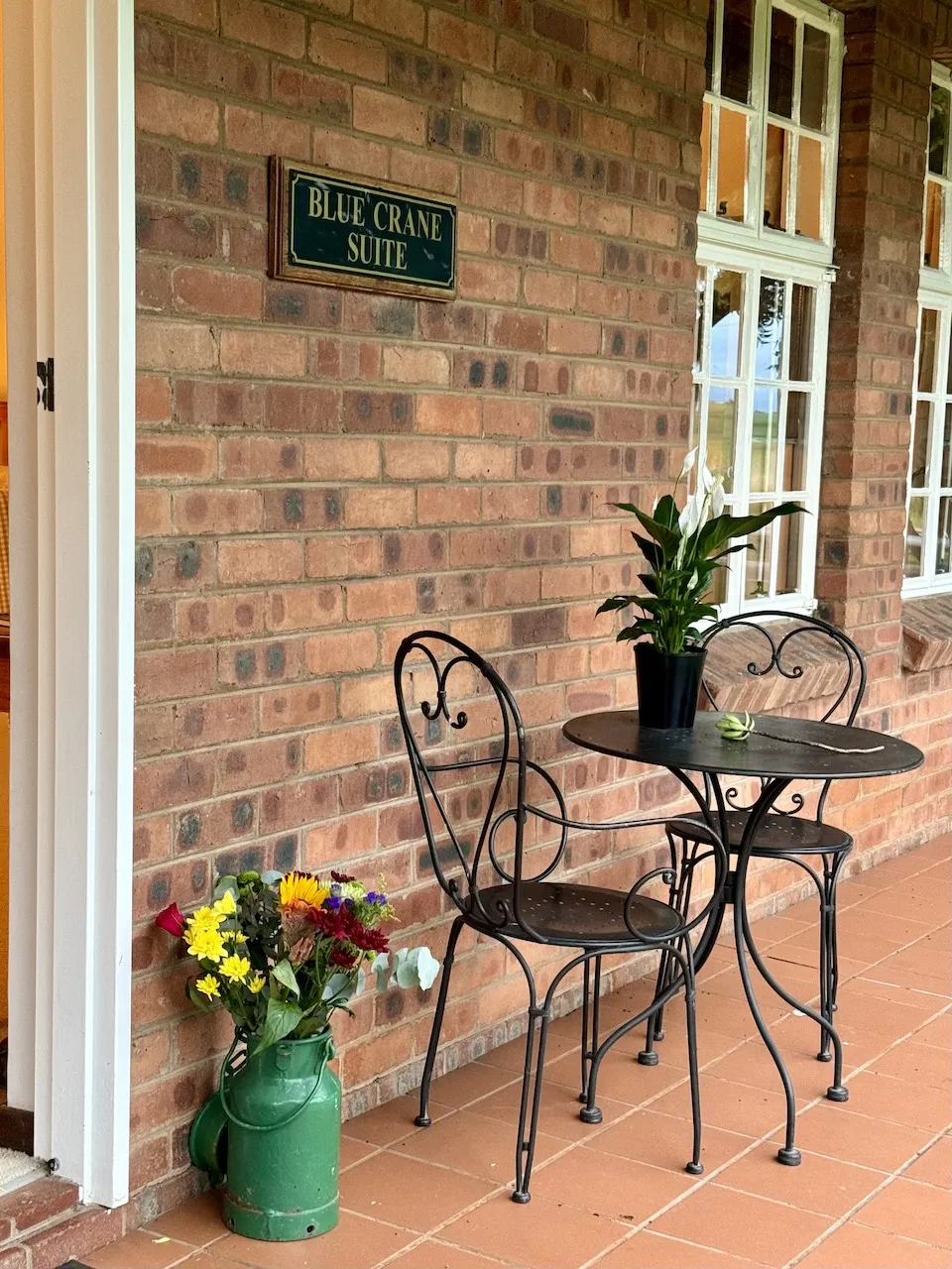 Brick wall with sign potted plant and table with chairs on tiled patio