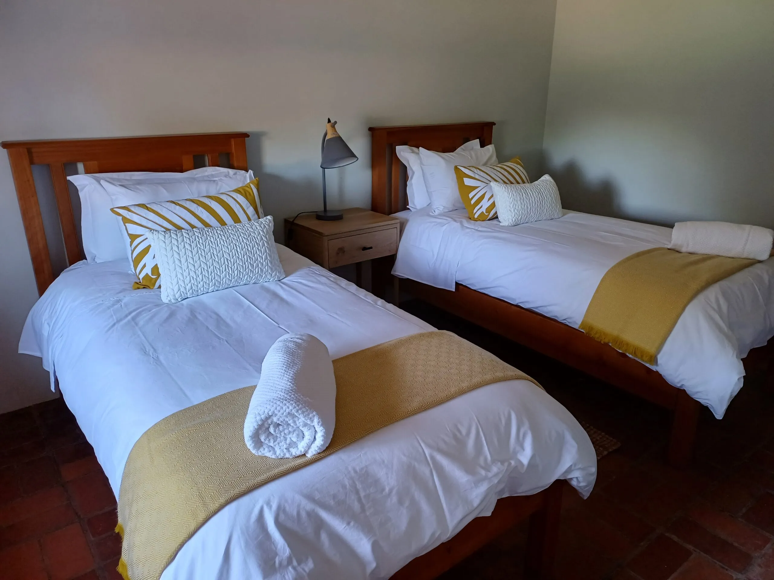 Two neatly made single beds in a tidy bedroom with yellow and white decor