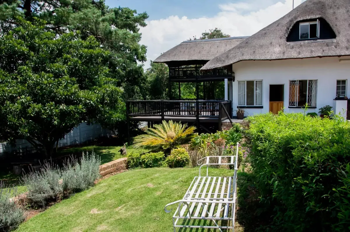 White bench in a lush garden beside a thatchedroof house with a balcony