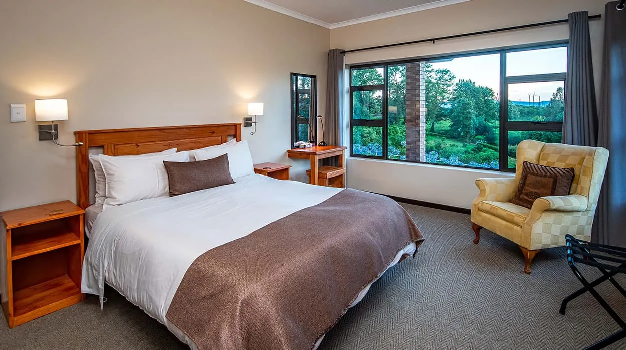 Cozy bedroom with large bed armchair and large windows overlooking a garden