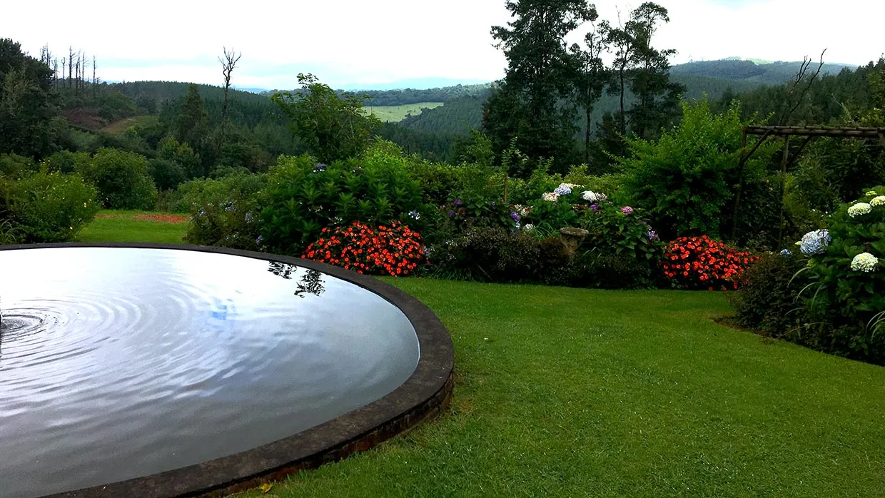 Circular pond in a lush garden with colorful flowers and distant hills