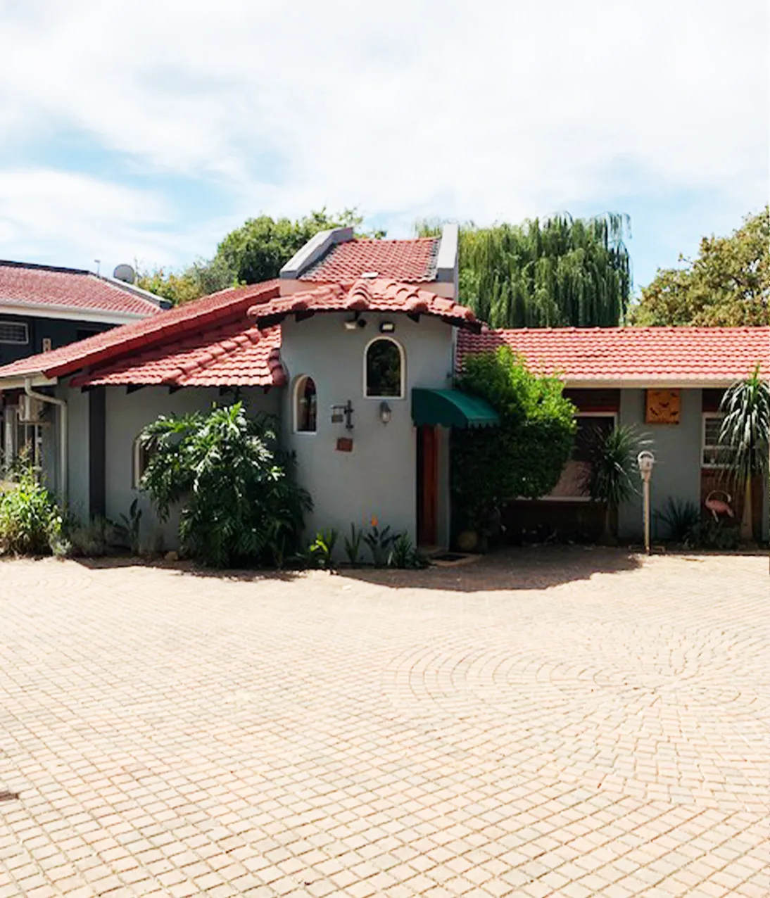 Singlestory house with redtiled roof and paved courtyard surrounded by greenery