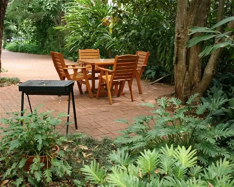Wooden table and chairs on a brick patio surrounded by lush greenery