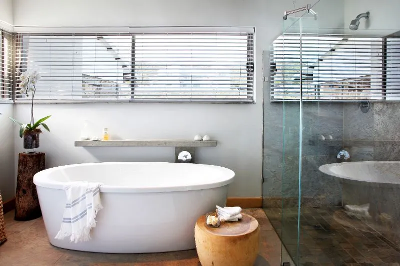 Modern bathroom with white bathtub wooden stool and glass shower enclosure