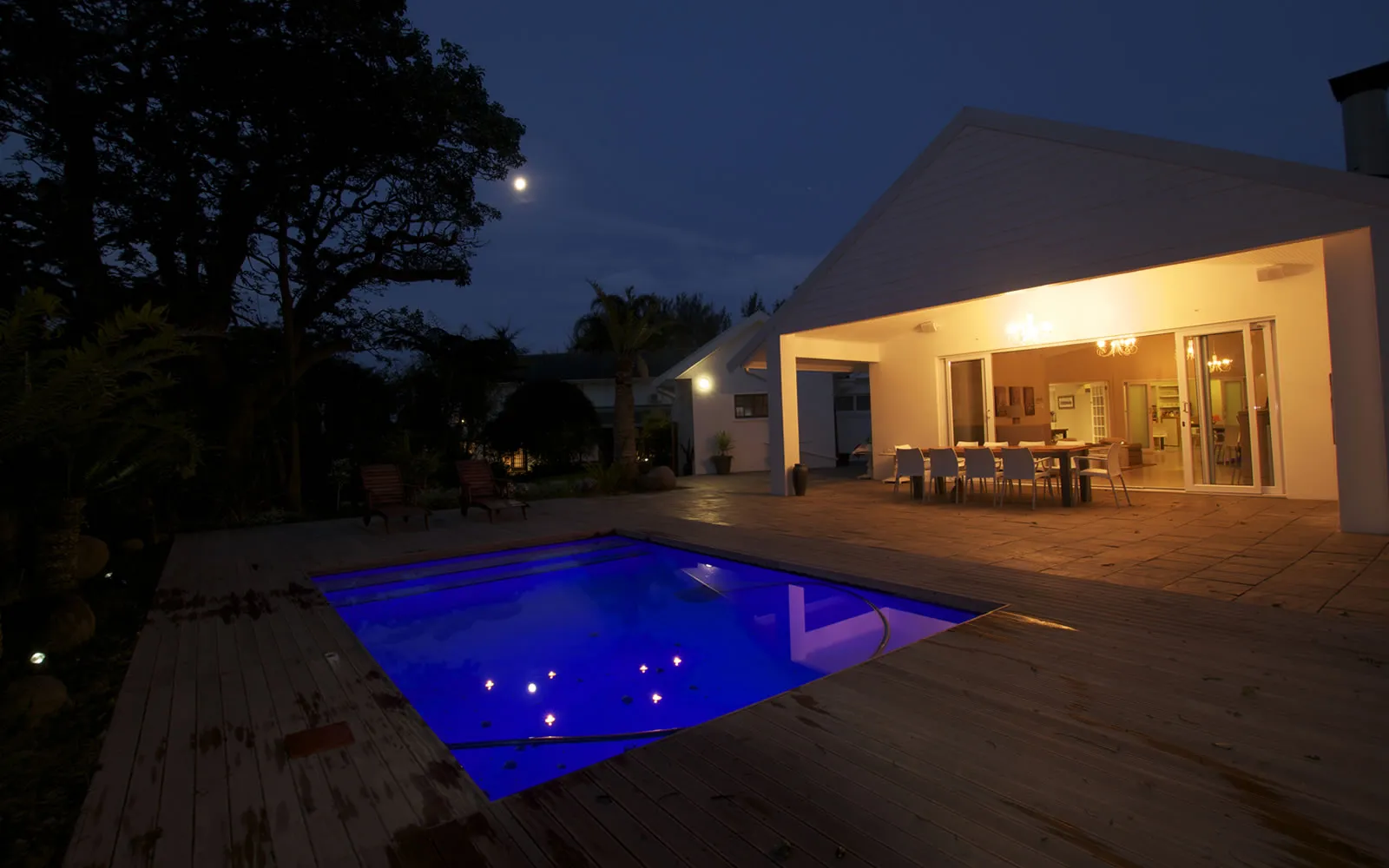 Modern house with lit pool and outdoor dining area at night