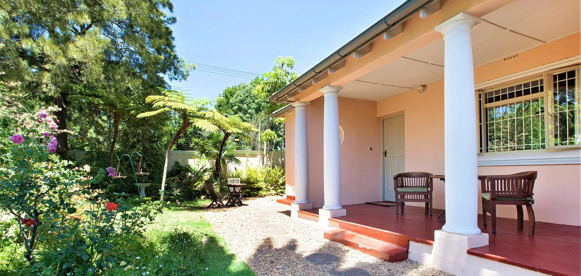 House with porch two chairs garden with flowers and trees in sunlight