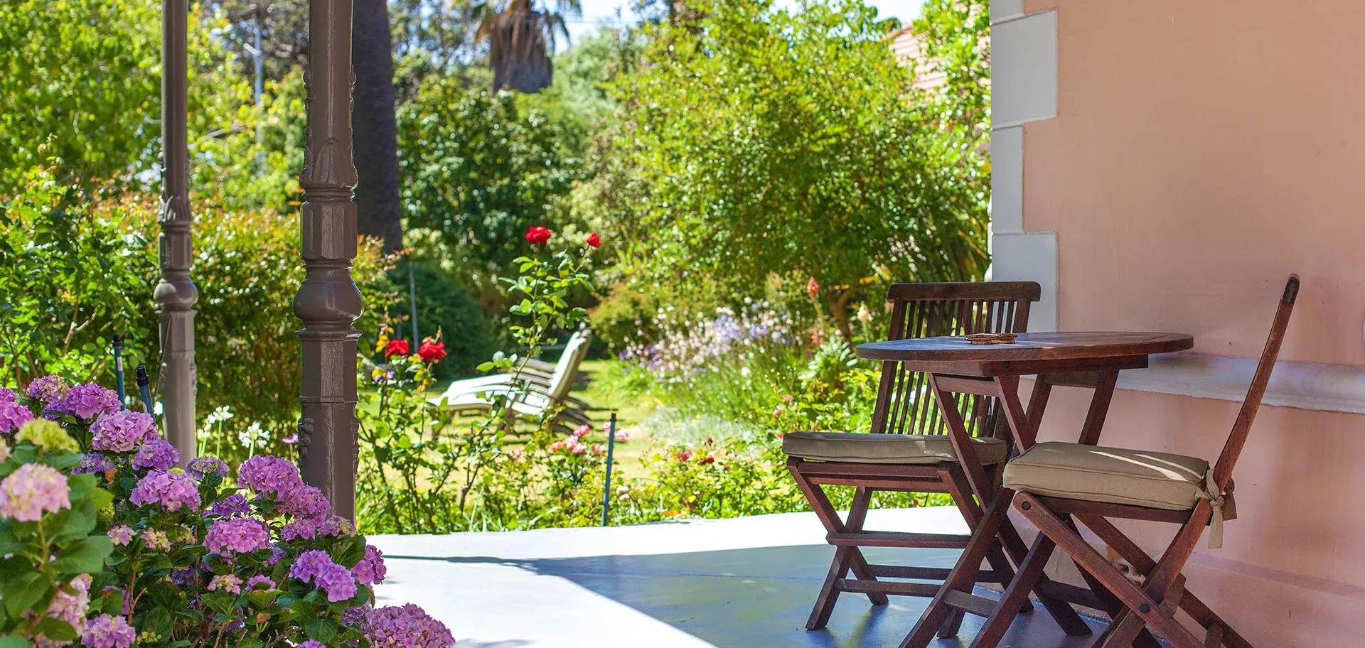 Wooden chairs and table on a patio with blooming flowers and greenery
