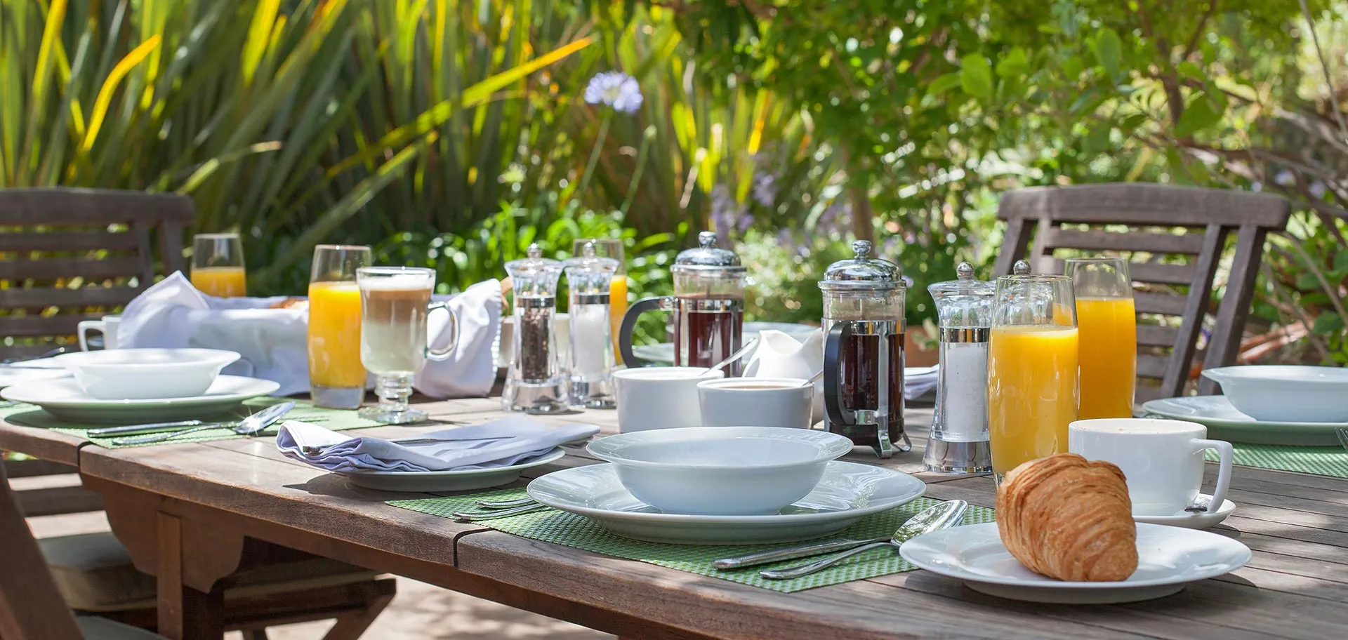 Outdoor breakfast table set with croissants juice and coffee in a garden