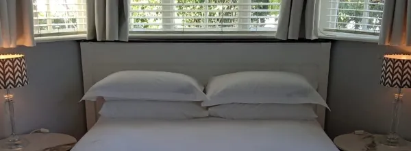 Bed with white pillows and bedding in a room with large windows and lamps