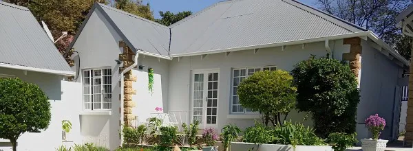 White house with grey roof surrounded by greenery and flowers