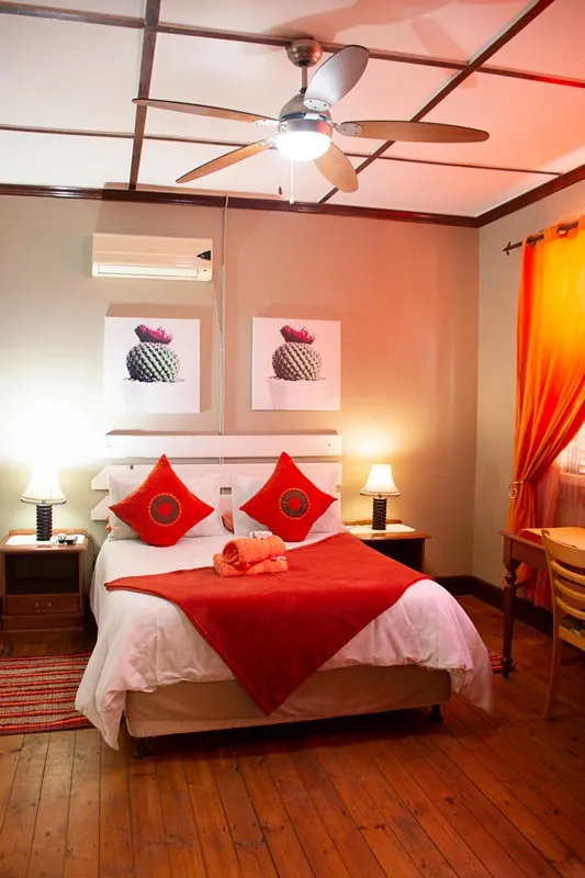 Bedroom with red and white bedding wooden floor ceiling fan and orange curtains