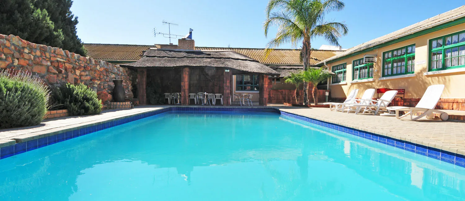 Swimming pool with lounge chairs palm trees and a building in the background