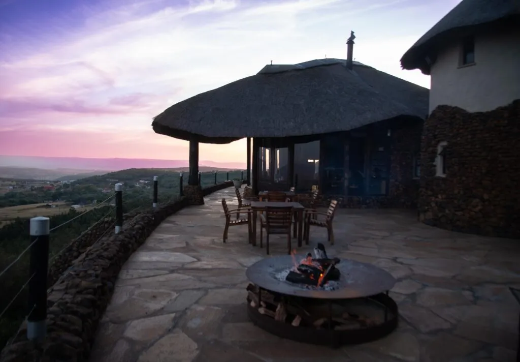 Thatchedroof house with outdoor seating and fire pit at sunset
