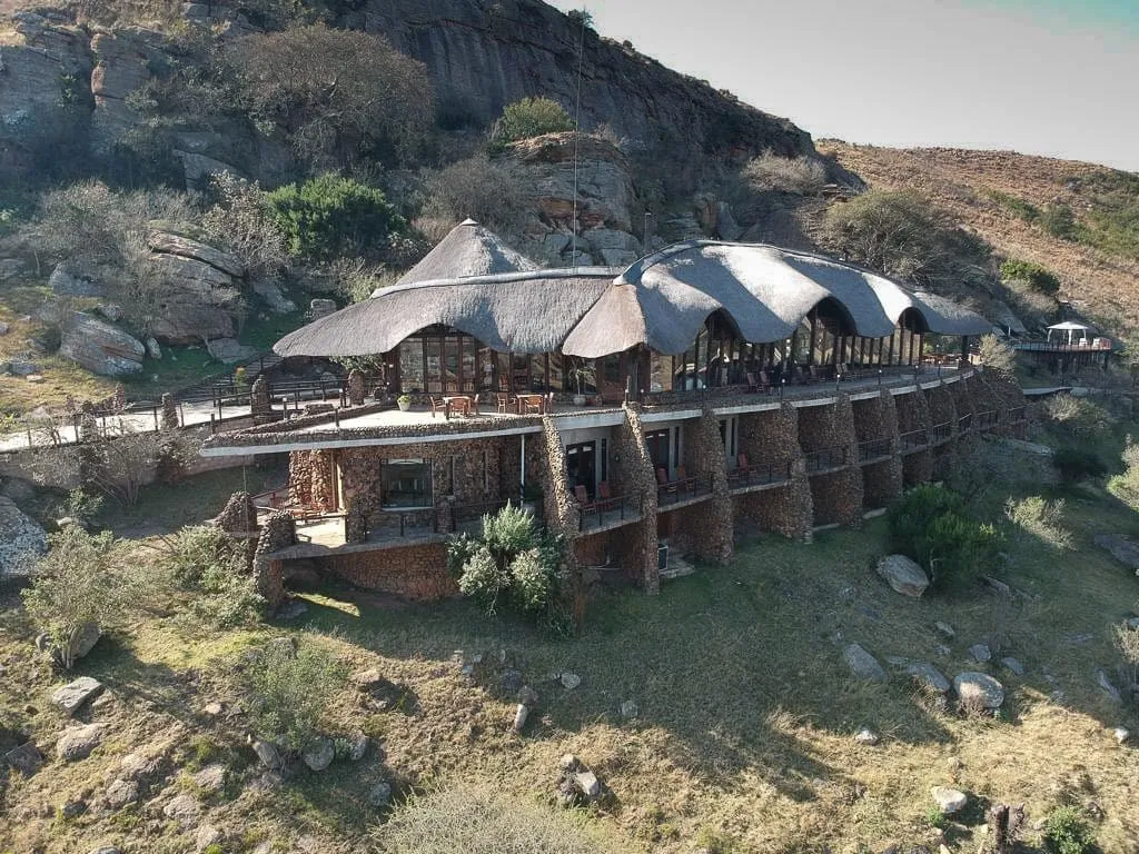 Rustic lodge with thatched roofs on a hillside surrounded by rocky terrain
