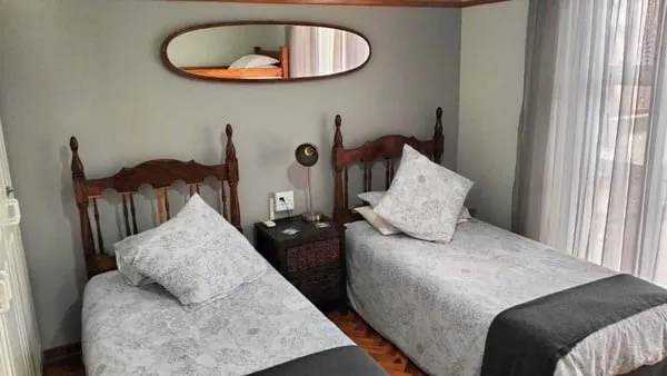 Two single beds with patterned bedding in a small bedroom with a mirror