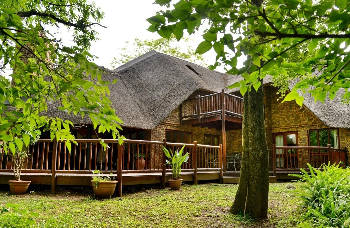 A large thatchedroof house with wooden balconies surrounded by greenery