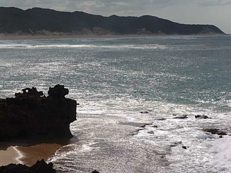 Rocky coastline with waves crashing against rocks and distant hills