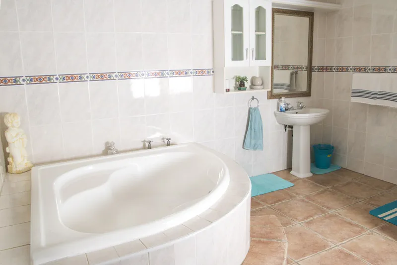White bathroom with bathtub sink mirror and blue towels on tiled floor