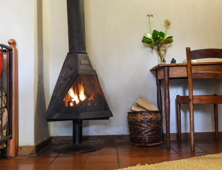 Wooden chair and table with a lit fireplace and basket of firewood