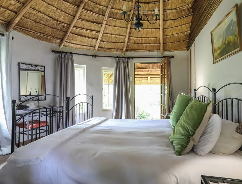 Cozy bedroom with a large bed green pillows and open windows to nature