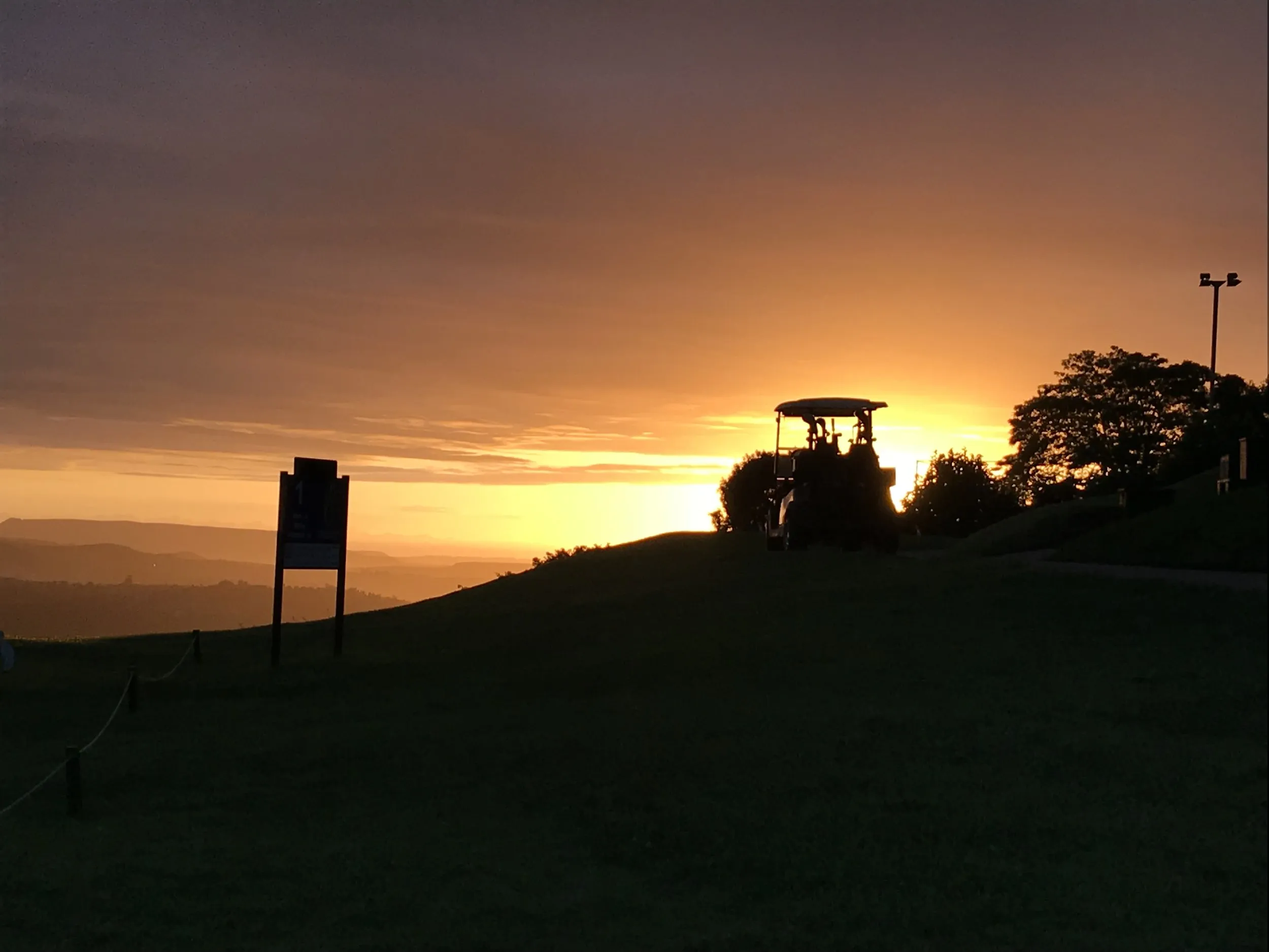 Silhouette of a tractor at sunset on a grassy hill