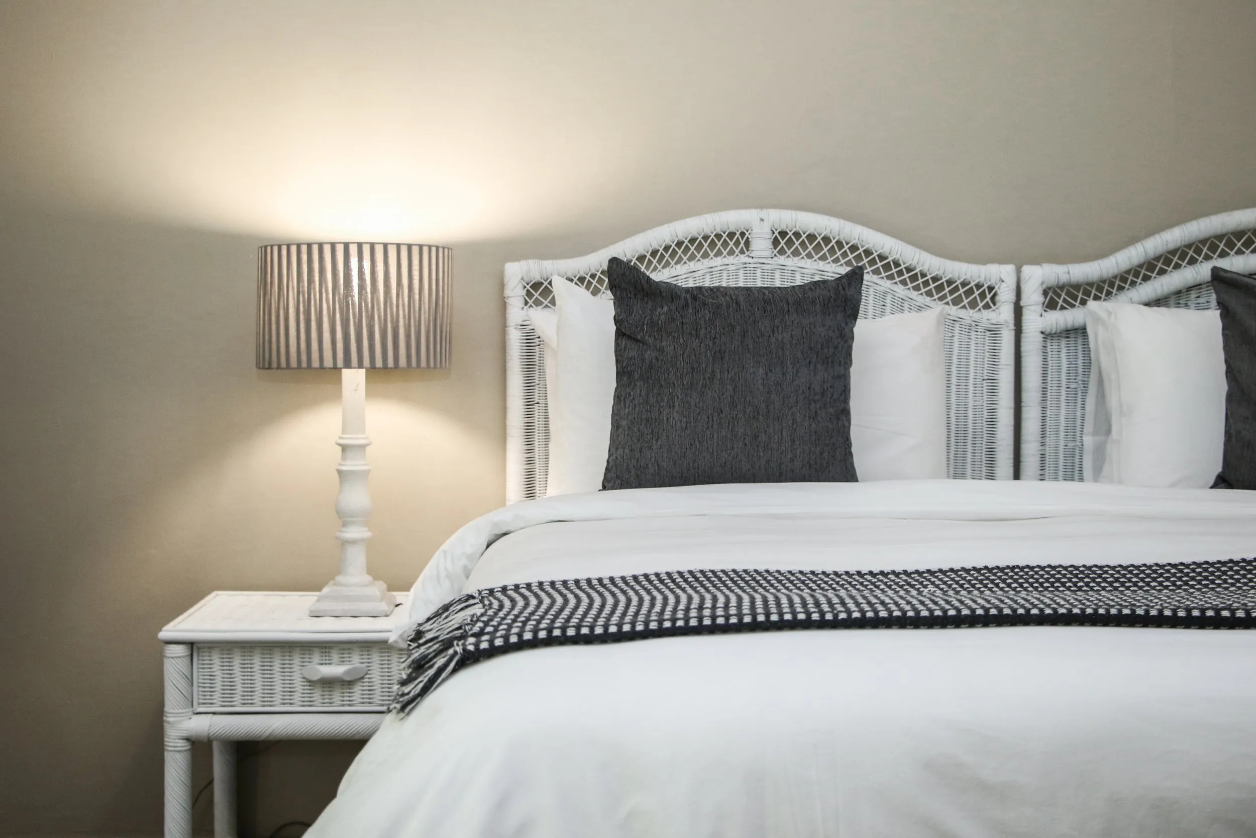 White bed with dark pillows white headboard and bedside lamp on wooden nightstand