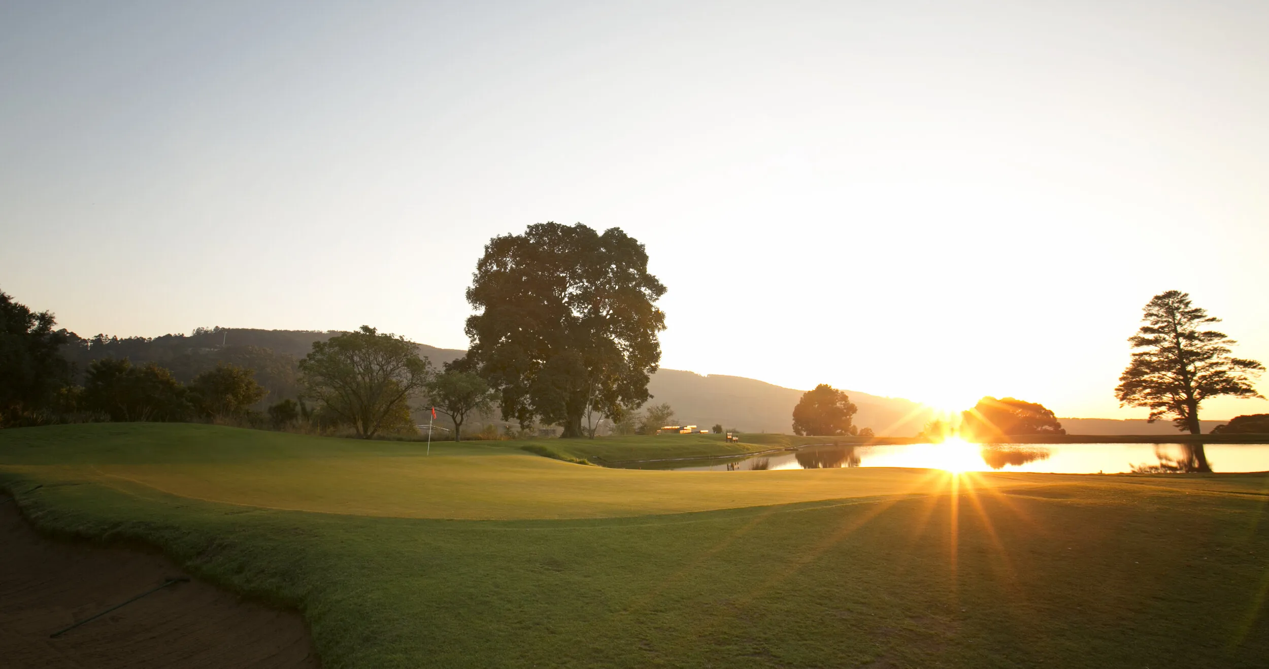 Golf course with trees and a lake at sunset
