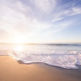 Beach with waves gently hitting the shore under a bright partly cloudy sky