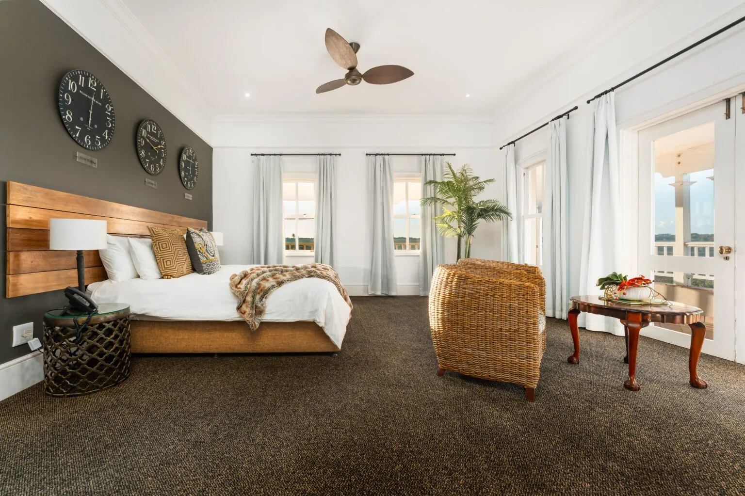 Bedroom with large bed ceiling fan wicker chair and large windows with curtains