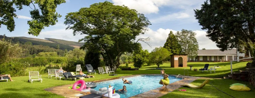 People relaxing by a pool in a lush green countryside setting