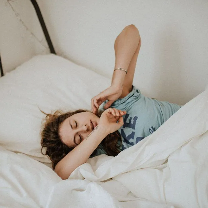 Woman stretching in bed with white sheets and a blue shirt