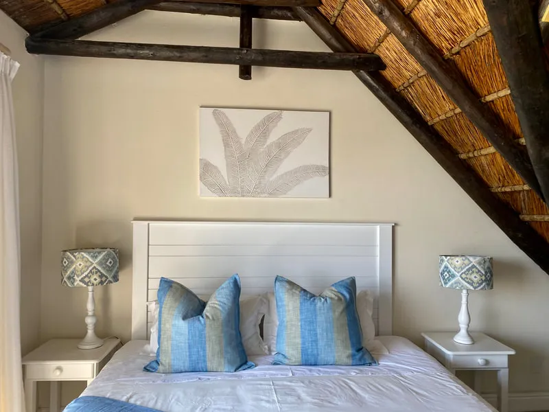 Bedroom with white bed blue and white pillows and a leaf artwork above