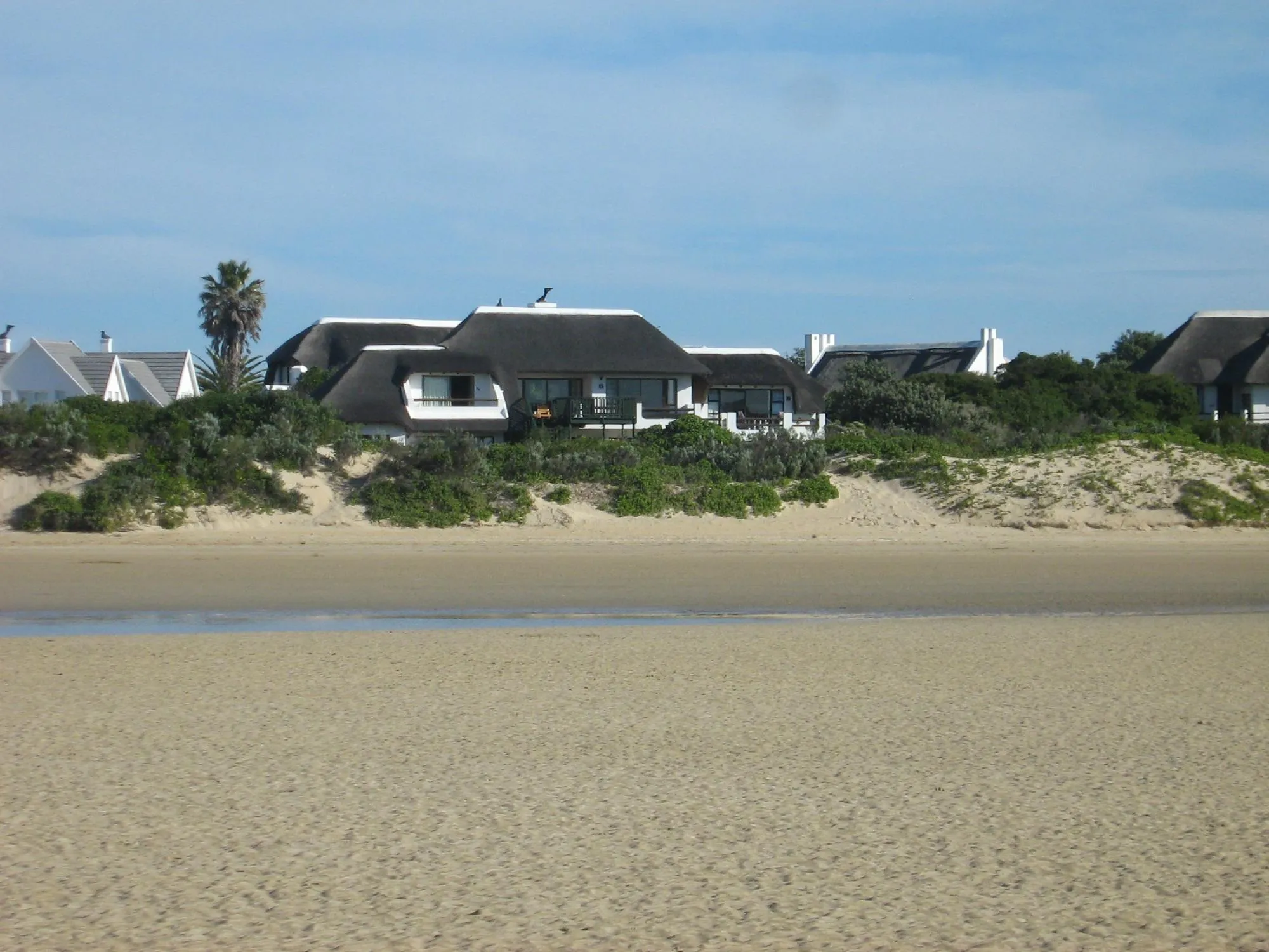 Beachfront houses with thatched roofs and sand dunes in the background