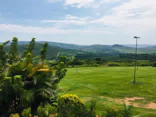 Green field with trees and hills under a partly cloudy sky