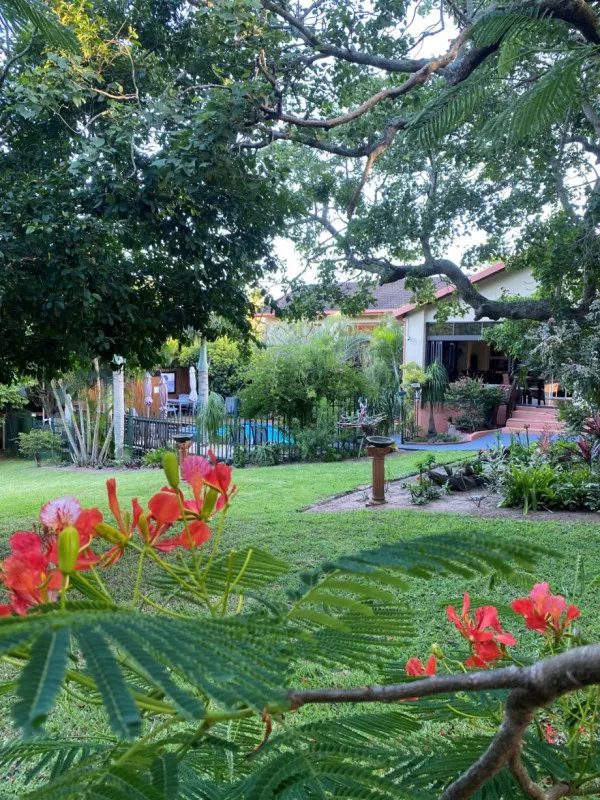 House with garden green trees and red flowers in foreground