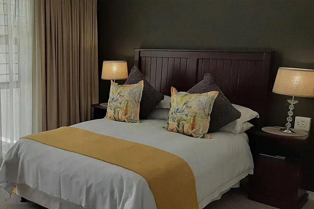 Neatly made bed with colorful pillows in a dark bedroom with bedside lamps