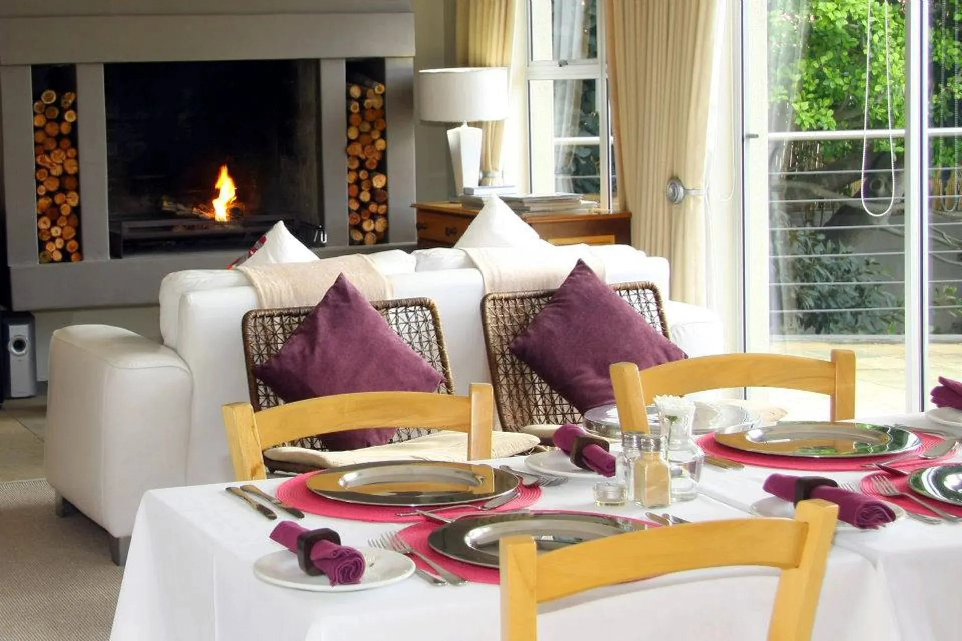 Dining table set for four with a cozy fireplace and large windows in background