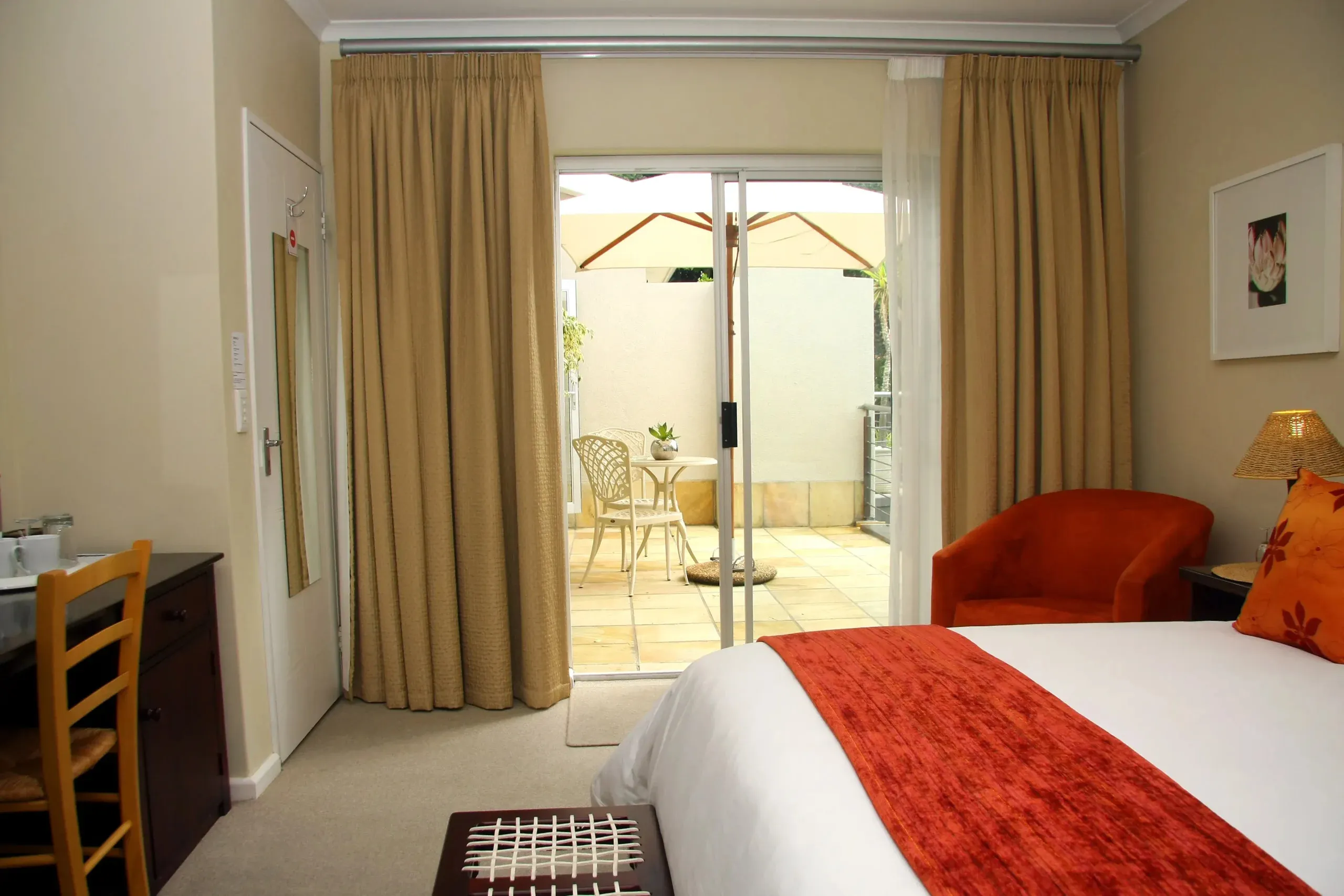Bedroom with orange accents sliding glass door to patio and beige curtains