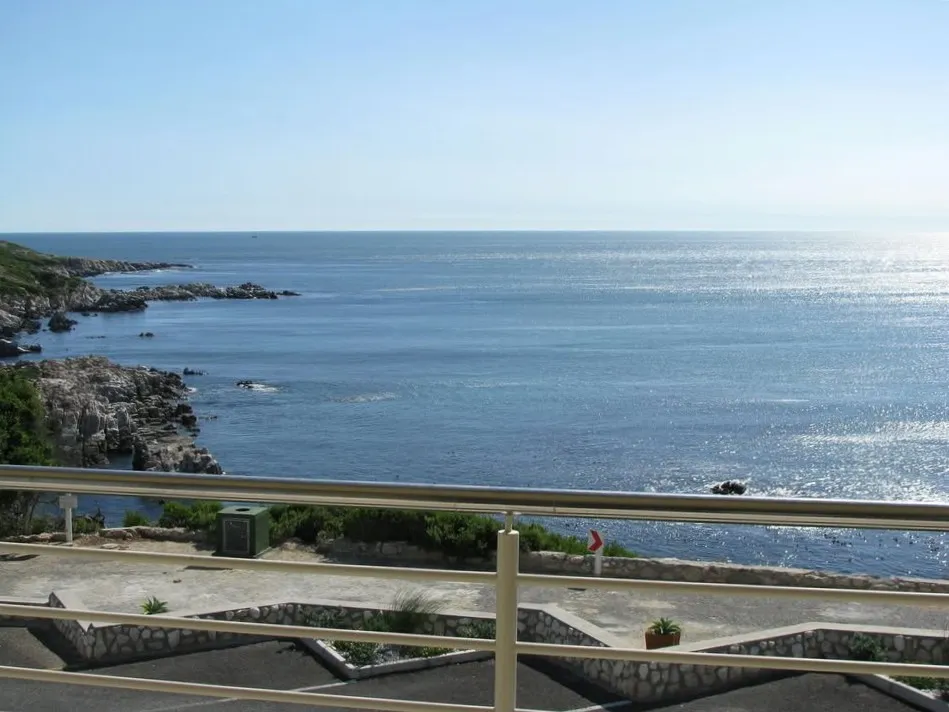 Ocean view from a balcony with a metal railing and stone walls