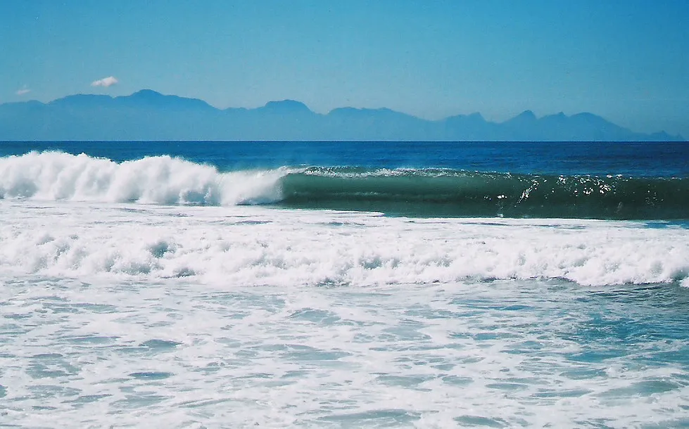 Ocean waves crashing with mountains in the background under a clear blue sky