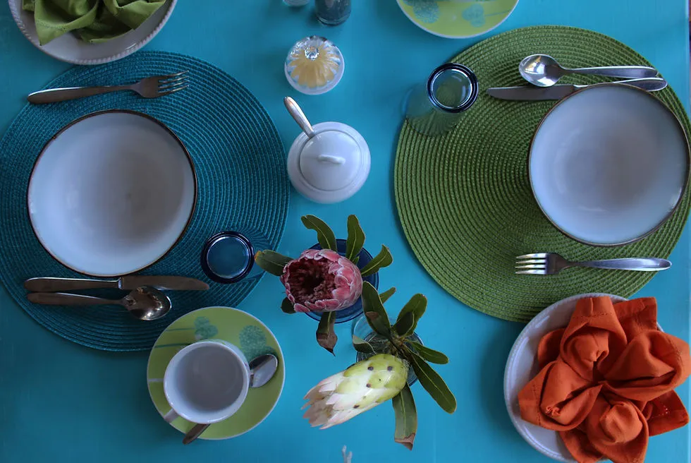 Two place settings with plates cutlery cups and a floral centerpiece on a blue table