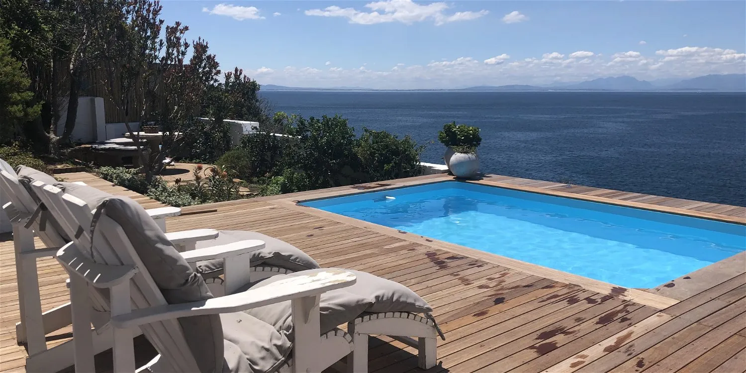 Wooden deck with lounge chairs overlooking a pool and ocean view