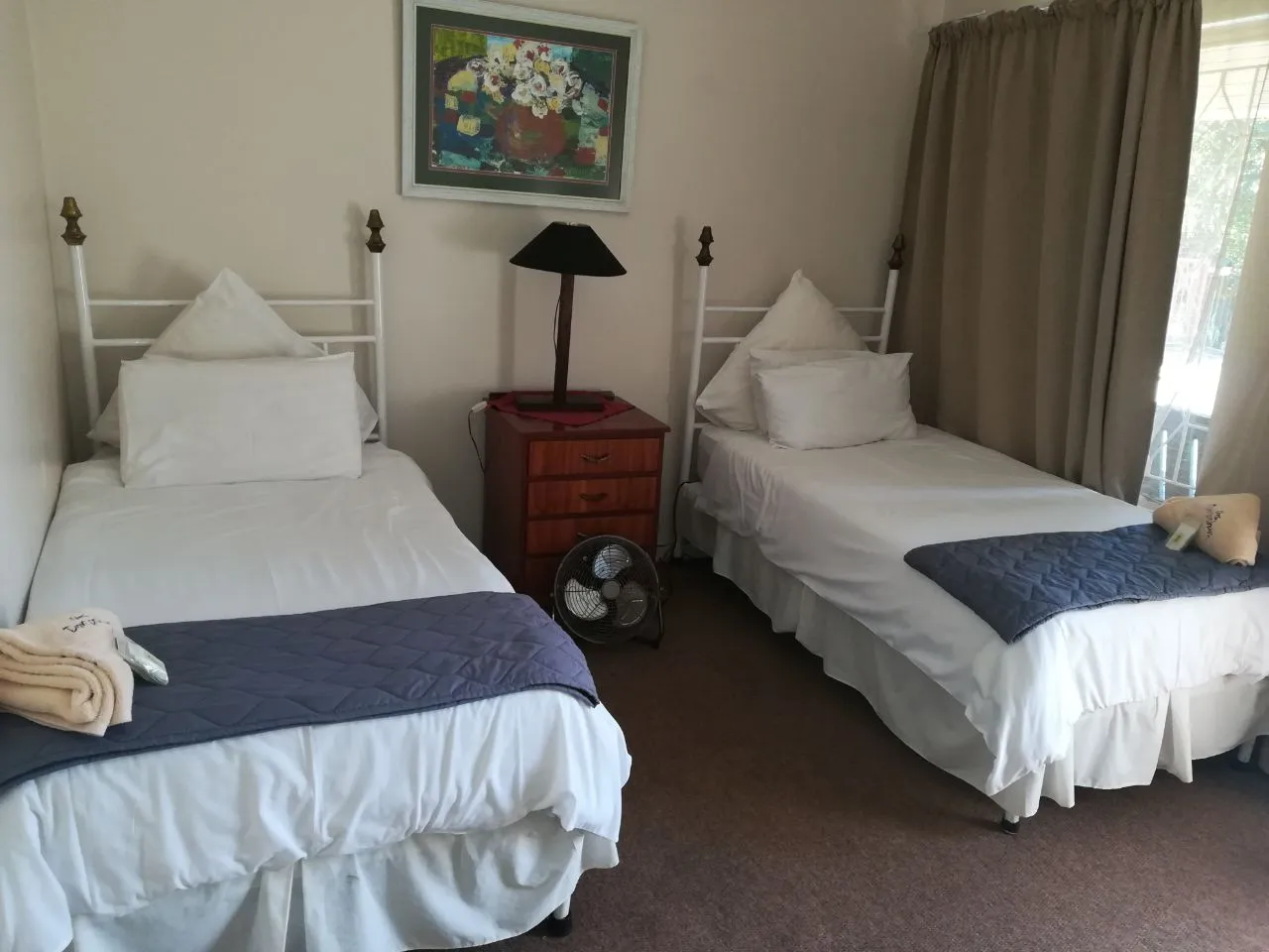 Two single beds in a tidy bedroom with a nightstand and a fan
