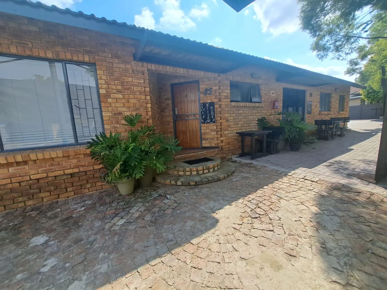 Brick building with wooden door potted plants and cobblestone pathway in sunlight