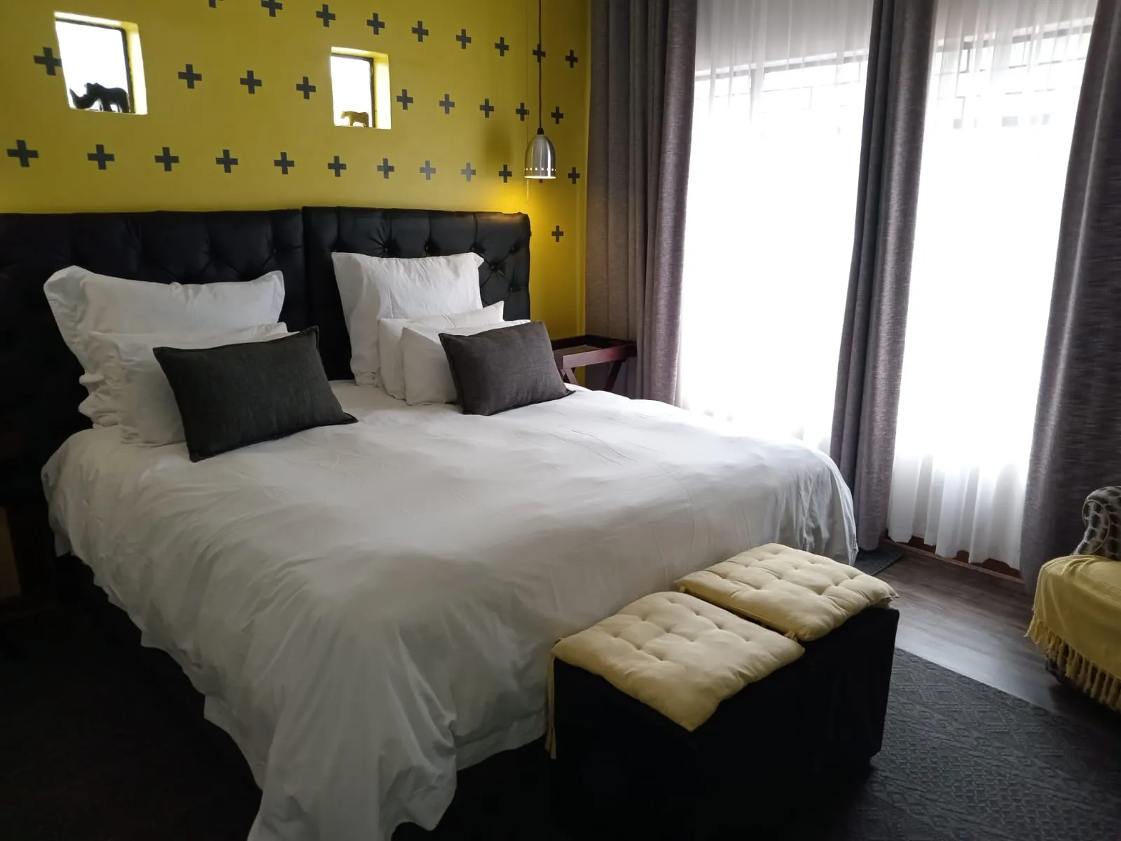 Modern bedroom with large bed yellow ottomans and large windows with curtains