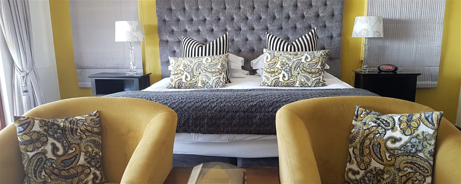 Bedroom with a large bed patterned pillows and two yellow armchairs