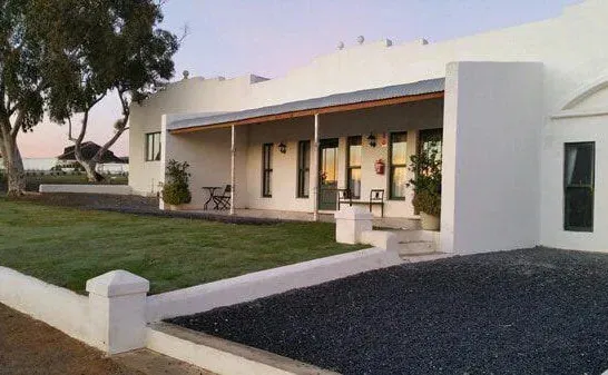 White house with covered porch green lawn and gravel driveway at sunset