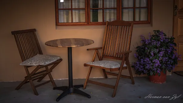 Two wooden chairs and a table on a patio with a potted plant