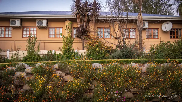 A peachcolored building with air conditioners and a garden in front