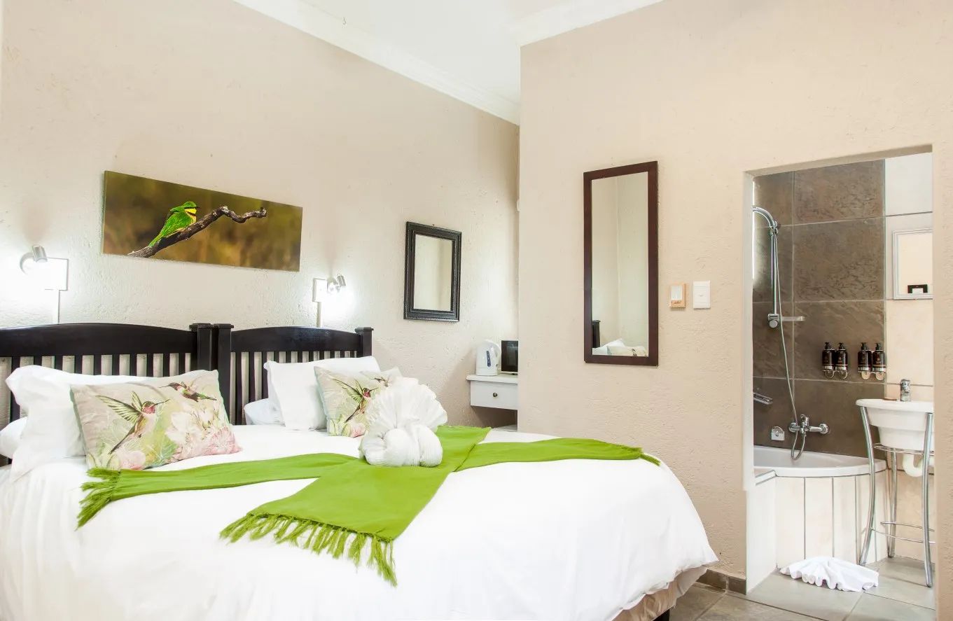 Bedroom with a bed green throw and an open bathroom with a shower